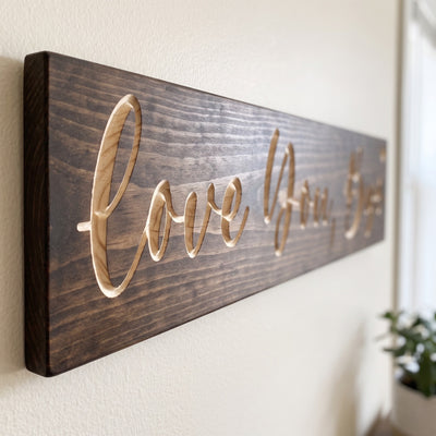 Close-up of the carved letters on the Love You, Bye sign, natural pine inside the cuts against the stained grain