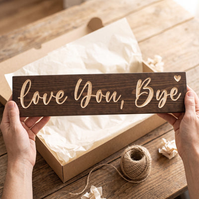 Hands holding the Love You, Bye sign over a kraft gift box with tissue paper