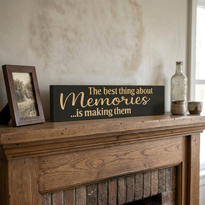 A dark Making Memories Sign with bare-wood lettering rests on a rustic wooden mantel, next to a framed picture and glass bottles, from Bluegrass Gifts