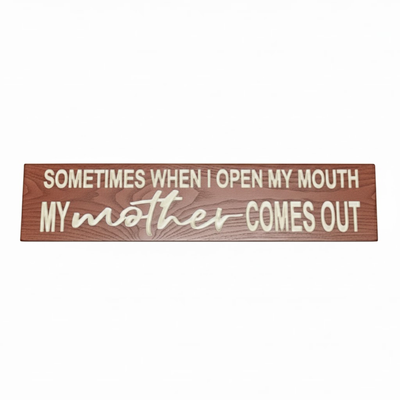 Flat lay view of a "Sometimes When I Open My Mouth My Mother Comes Out" carved wood sign on a white background.