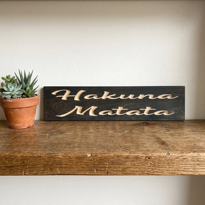 A dark No Worries Sign with light carved letters rests on a rustic wooden shelf next to a small potted succulent from Bluegrass Gifts
