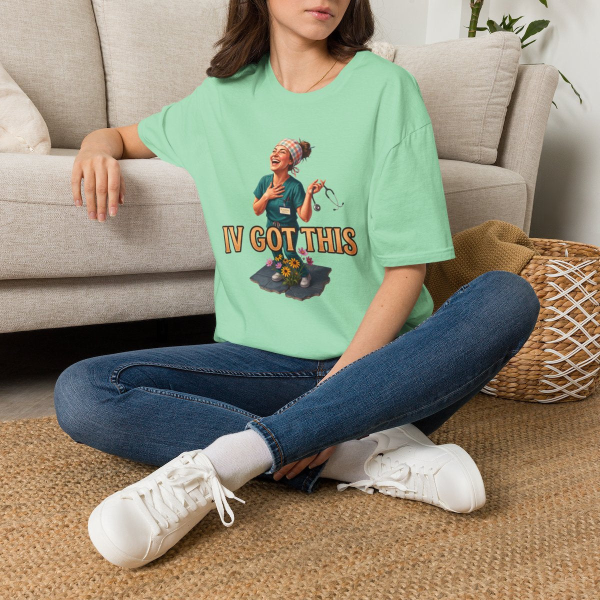 A woman sits cross-legged on a rug, wearing a mint green Nurse Shirt - IV Got This, next to a couch