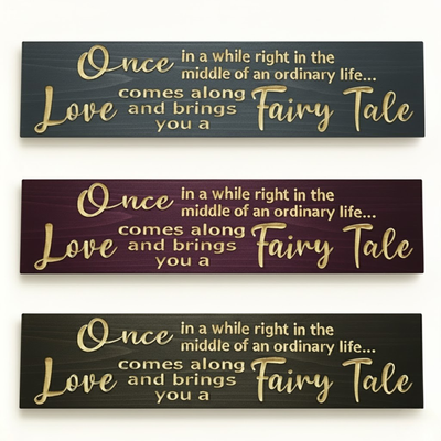 Three color variations of “Once in a while love brings you a fairy tale” carved wooden signs — multiple finishes including black, burgundy, and gray tones.