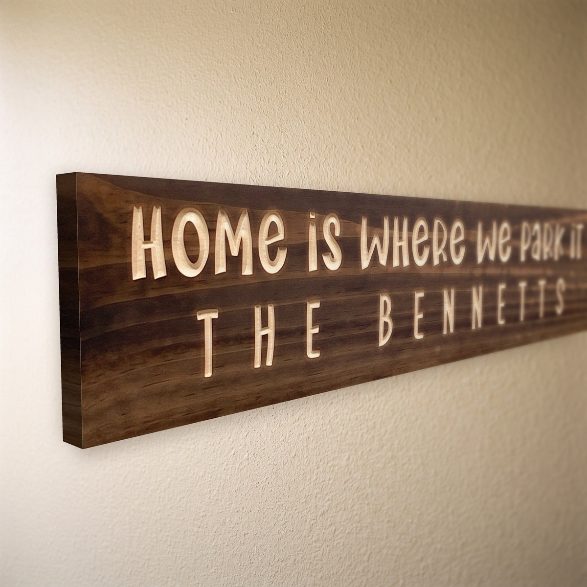 Close-up of the carved letters on the Home Is Where We Park It sign, natural pine inside the cuts against the stained grain
