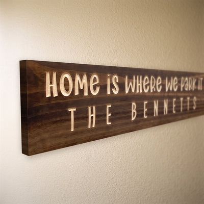 Close-up of the carved letters on the Home Is Where We Park It sign, natural pine inside the cuts against the stained grain