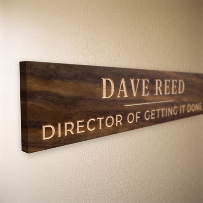Close-up of the carved letters on the Dave Reed sign, natural pine inside the cuts against the stained grain