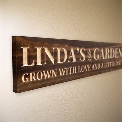 Close-up of the carved letters on the Linda's Garden sign, natural pine inside the cuts against the stained grain