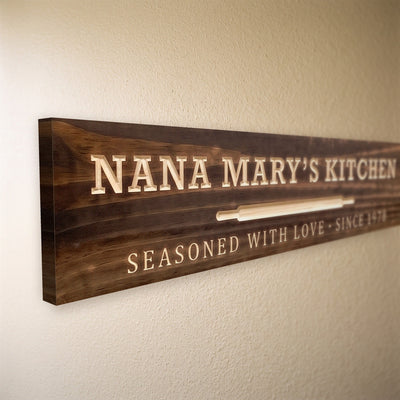 Close-up of the carved letters on the Nana Mary's Kitchen sign, natural pine inside the cuts against the stained grain