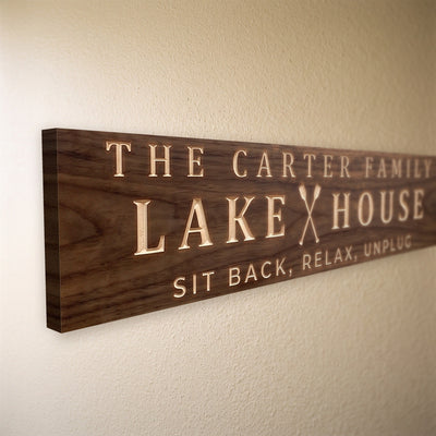 Close-up of the carved letters on the The Carter Family Lake House sign, natural pine inside the cuts against the stained grain
