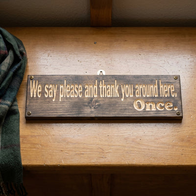 A dark wood House Rules Sign with carved light letters hangs on a wooden wall next to a green plaid scarf from Bluegrass Gifts