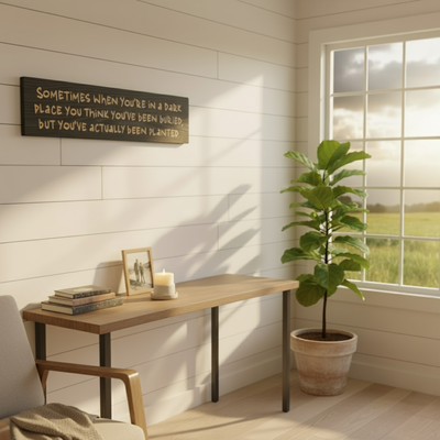 A carved wood resilience sign hanging on a white shiplap wall in a modern farmhouse home office, creating a mindfulness corner with a desk, chair, and a large fiddle-leaf fig plant.