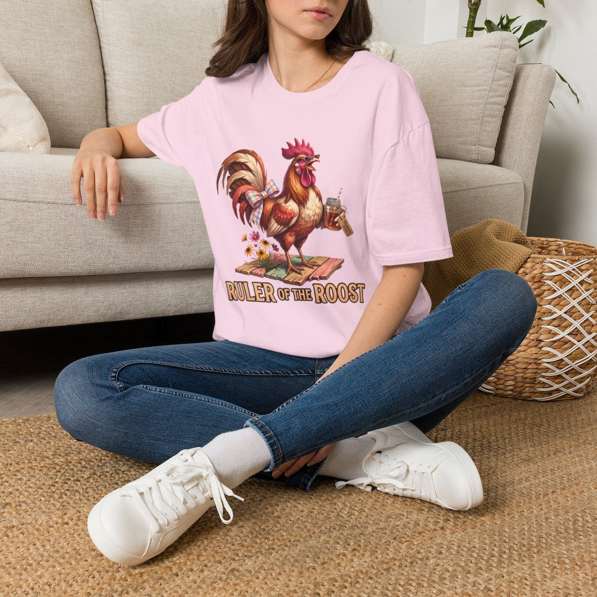 A woman sits on a rug, wearing a light pink oversized Rooster Shirt - Ruler of the Roost, from Bluegrass Gifts