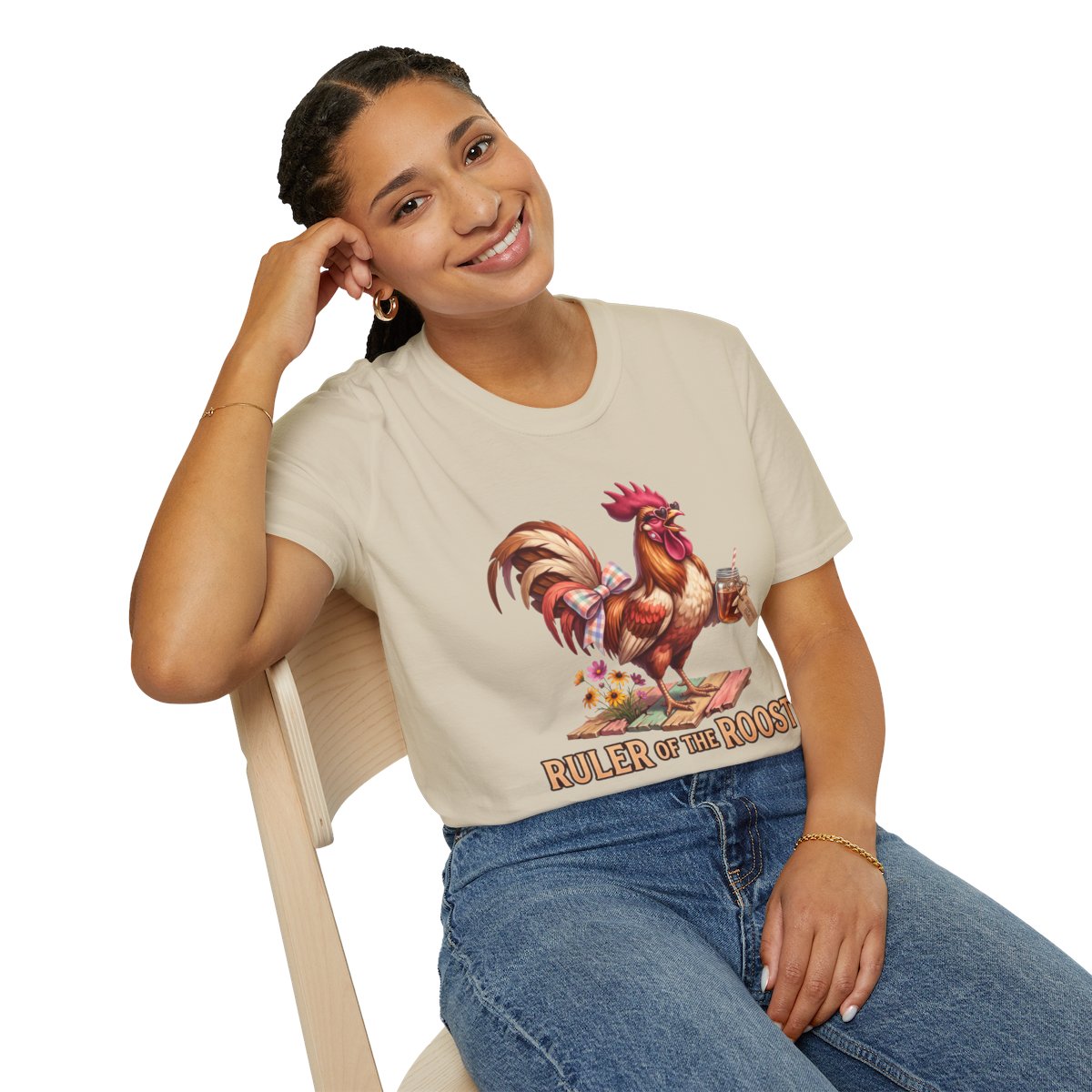 A woman seated and smiling, displaying the full graphic on her beige Rooster Shirt - Ruler of the Roost