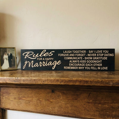 A Rules for a Happy Marriage Sign sits on a wooden mantelpiece next to a framed wedding photo from Bluegrass Gifts