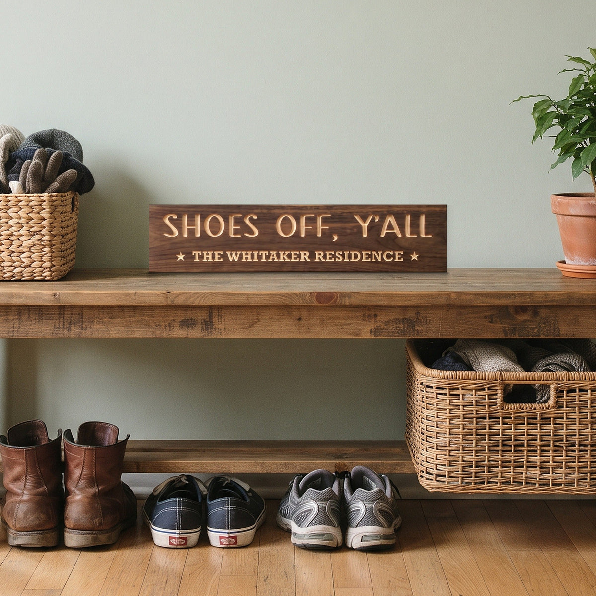 Shoes Off, Y'all personalized wood sign standing on a mudroom bench beside a basket of gloves and a potted plant, with shoes underneath