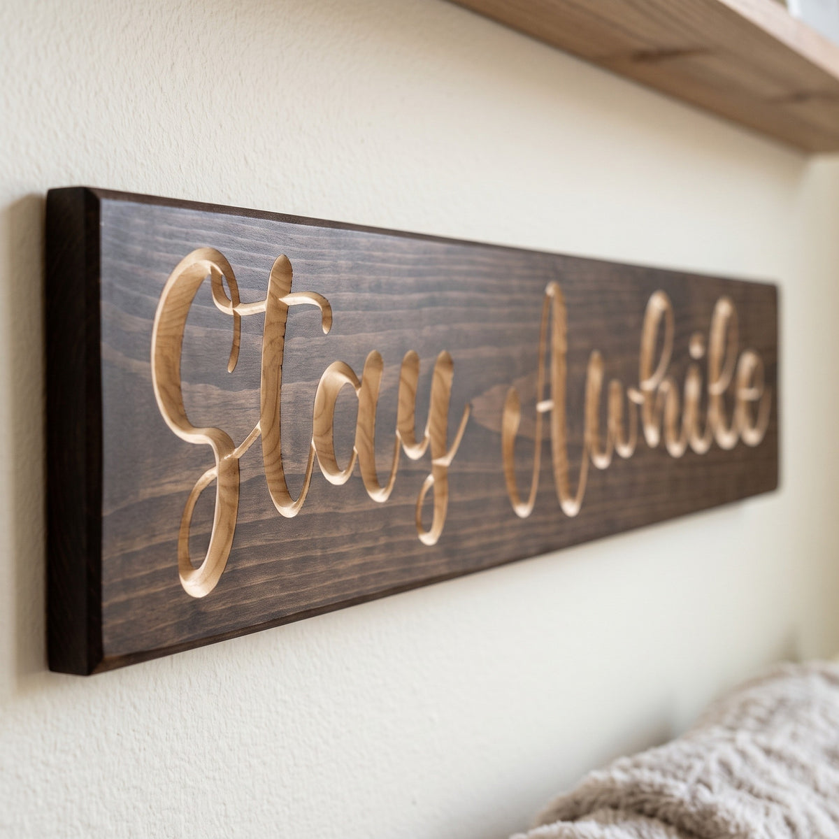 Close-up of the carved letters on the Stay Awhile sign, natural pine inside the cuts against the stained grain