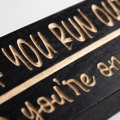 Close-up macro of deeply CNC-carved lettering on the Text Me If You Run Out of TP funny bathroom sign showing dimensional 2.5D routing through Ebony stain