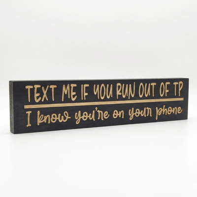 Angled view of the Text Me If You Run Out of TP funny bathroom sign showing dimensional CNC-carved letters and rich Ebony stain on solid Pine
