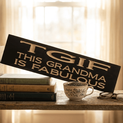 TGIF This Grandma Is Fabulous funny wood sign displayed on a rustic shelf with vintage books, teacup, and reading glasses in warm window light