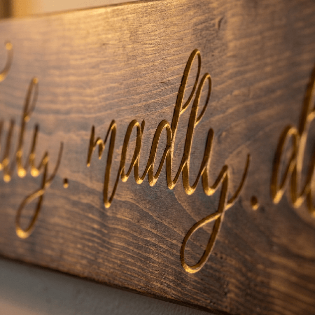 Macro close-up of the deep CNC-carved gold script lettering on the Truly Madly Deeply wood sign, showing fine calligraphy detail and natural wood grain