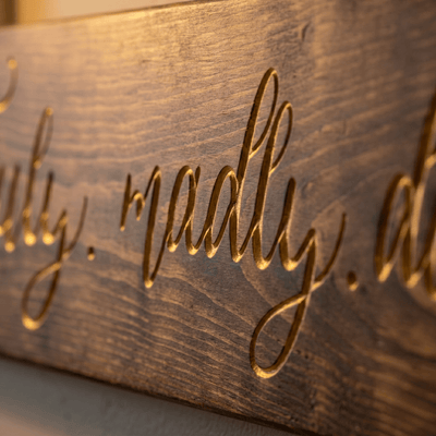 Macro close-up of the deep CNC-carved gold script lettering on the Truly Madly Deeply wood sign, showing fine calligraphy detail and natural wood grain