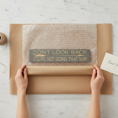 Overhead unboxing shot of the "Don't Look Back" sign being wrapped in eco-friendly packaging, showcasing a gift-ready presentation.