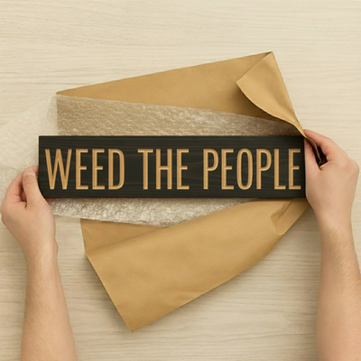 Hands unboxing a "Weed The People" wood sign from kraft paper and bubble wrap, revealing the carefully packaged handmade product.