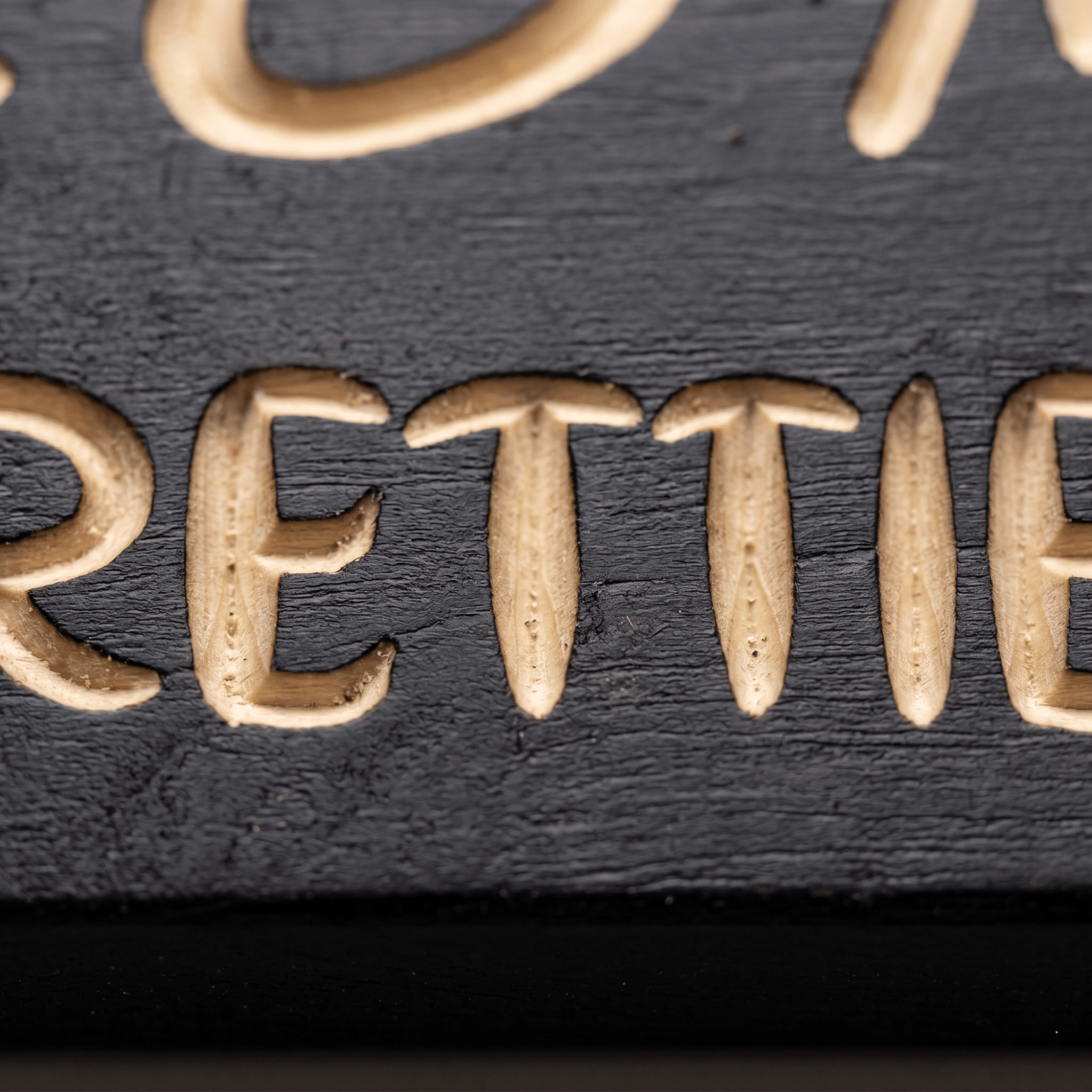 Macro close-up of CNC-carved my pretties letters revealing natural pine beneath the black finish.