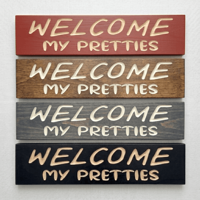 Four Welcome My Pretties Halloween signs in barn red, walnut, gray, and black finishes.