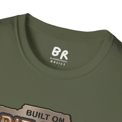 A close-up of the collar of an olive green t-shirt shows the BR Bluegrass Roots Basics tag above the Welding Shirt - Built on Grit & 6011 design