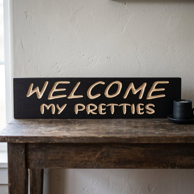 A black Witch Welcome Sign with carved light wood letters rests on a rustic wooden table from Bluegrass Gifts