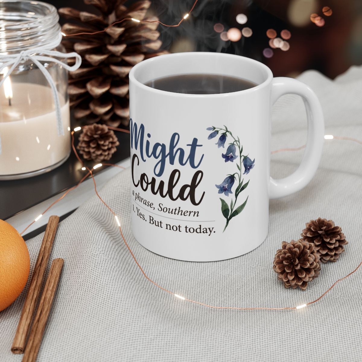 A white Mug With Sayings, filled with a dark beverage, sits on a festive table with pinecones and string lights