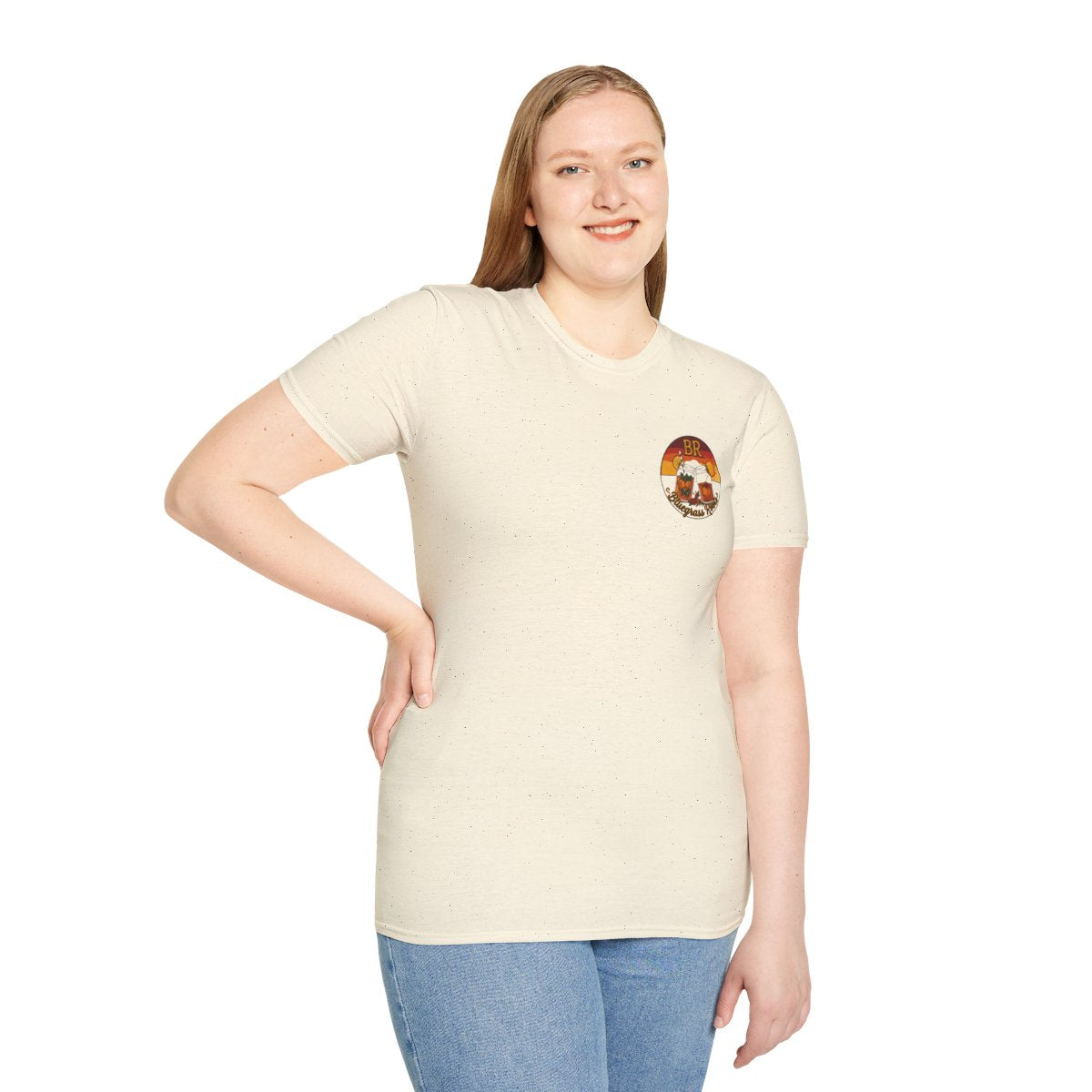 A woman smiling, standing and looking forward, wearing a light beige Hallelujah Shirt with the BR sunset badge on the chest