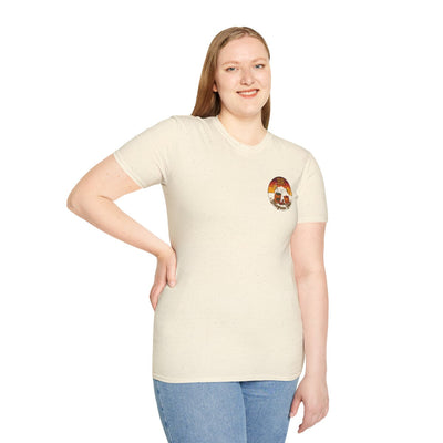 A woman smiling, standing and looking forward, wearing a light beige Hallelujah Shirt with the BR sunset badge on the chest