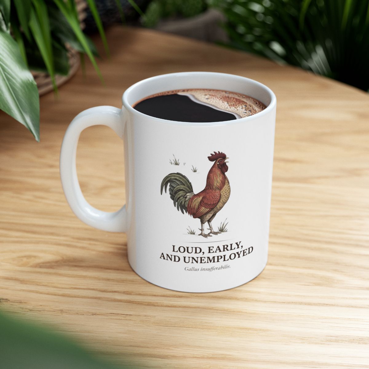 The Rooster Coffee Mug filled with coffee, sitting on a warm wooden table with green foliage visible in the background