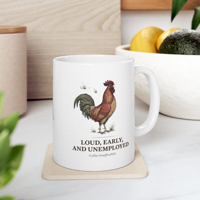 A white Rooster Coffee Mug on a light coaster, placed on a kitchen counter with a bowl of fruit and greenery in the background