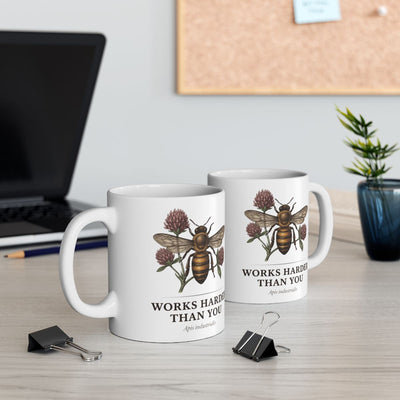 Two white Bee Coffee Mugs on a desk, one in front of a laptop, with office supplies and a plant in the background