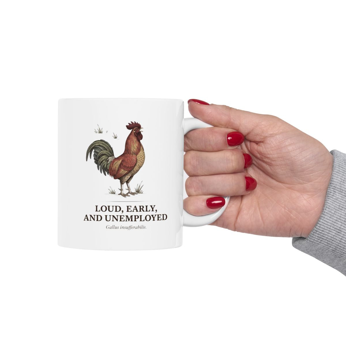 A hand with red painted nails holds the white Rooster Coffee Mug, extending it forward against a plain background