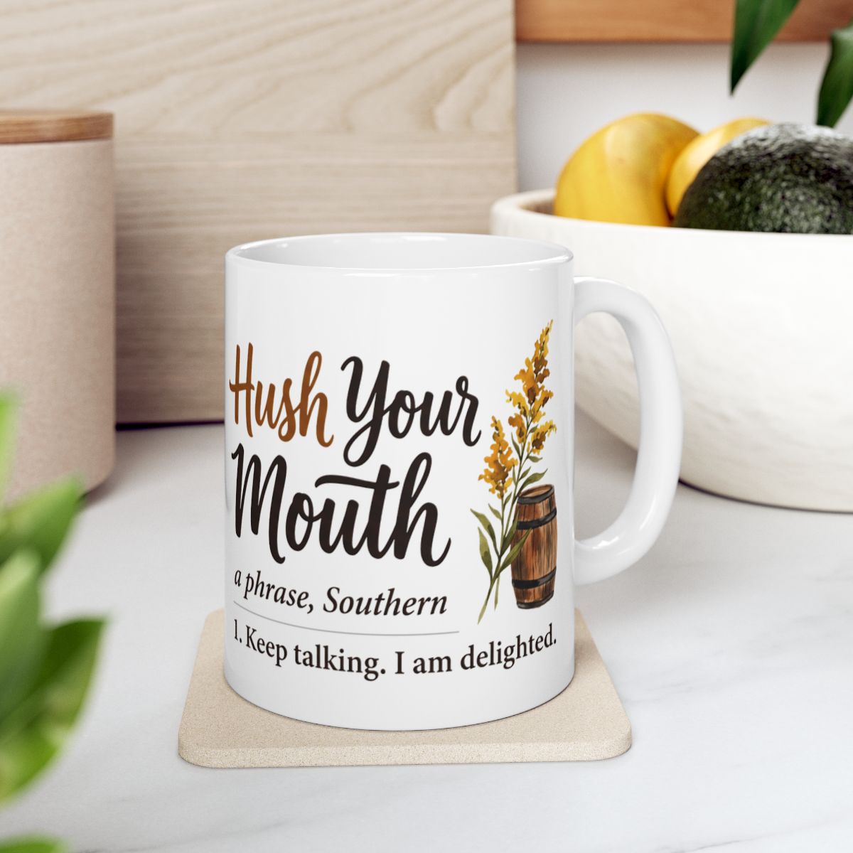 A white Kentucky Coffee Mug rests on a light coaster in a kitchen setting with fruit and wooden accents visible