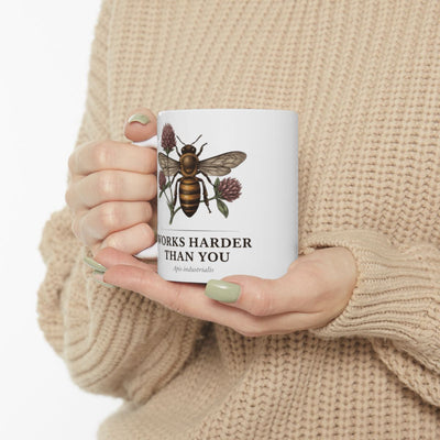 Hands with light green painted nails gently holding the white Bee Coffee Mug, against a soft, light-colored knitted sweater