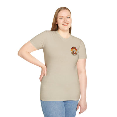A woman smiling, standing and looking forward, wearing a light tan Hallelujah Shirt with the BR sunset badge on the chest