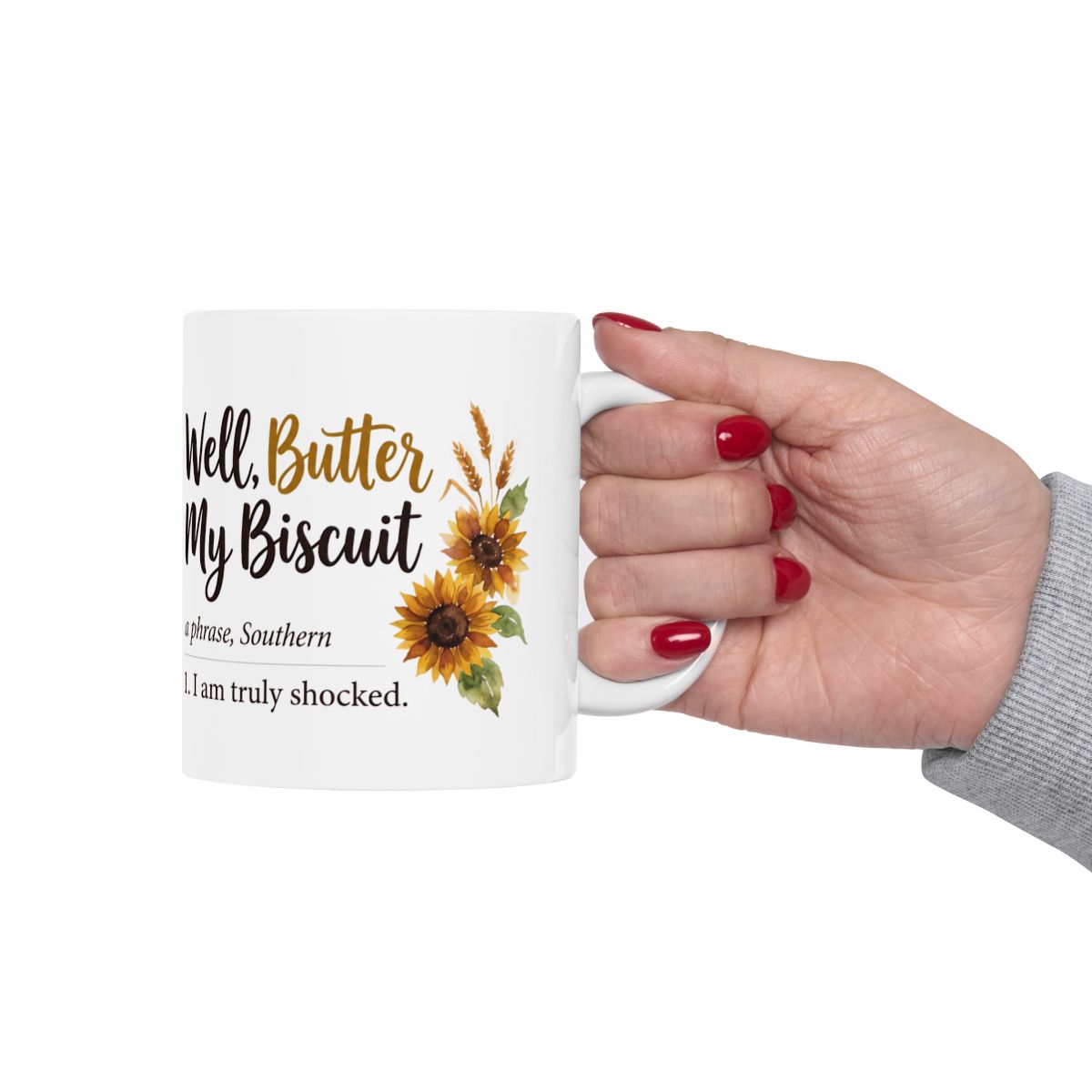 A hand with red nail polish holds a white ceramic mug by the handle, featuring the "Well, Butter My Biscuit" design, for Mugs for Women