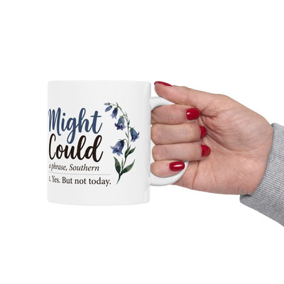 A hand with red painted nails holds the white Mug With Sayings, presenting the "Might Could" design against a white background
